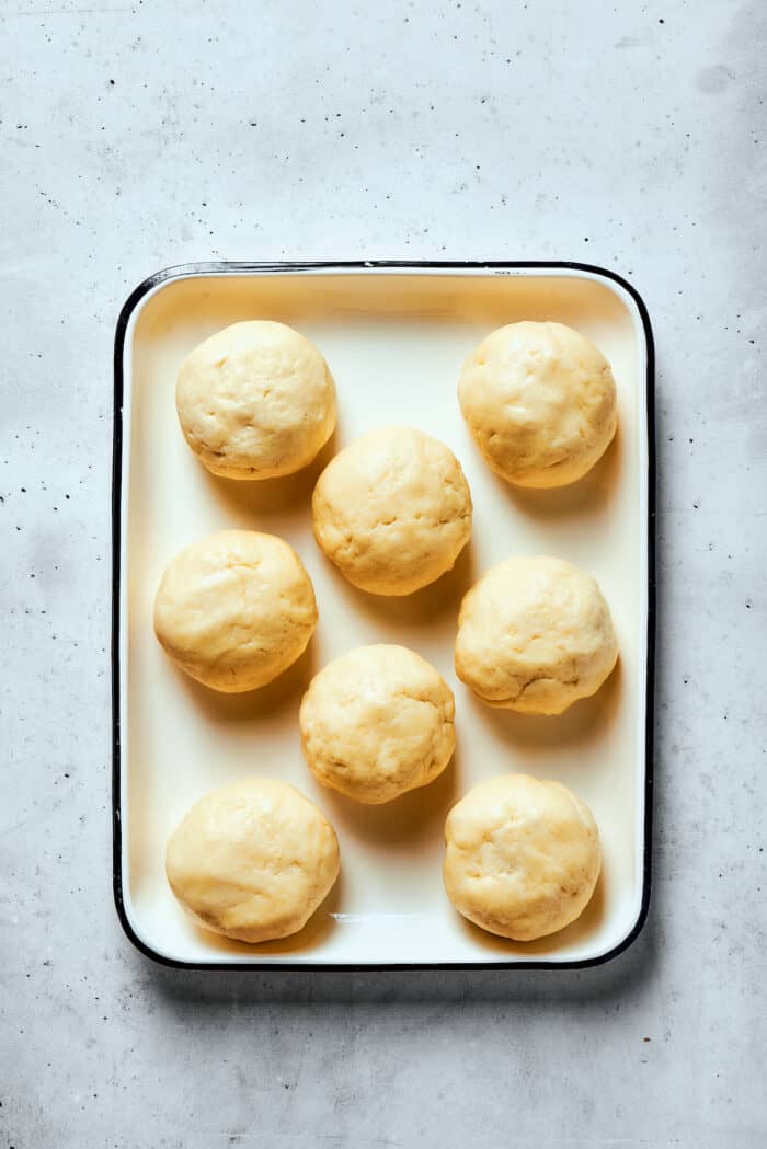 Eight balls of pastry dough are shown on a rimmed baking sheet.