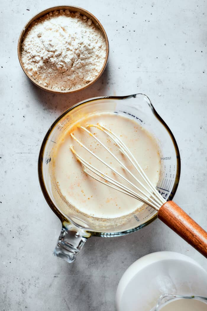 A glass cup full of pastry cream mix and a whisk.