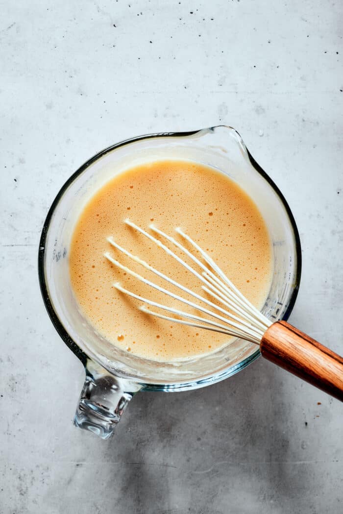 A glass measuring cup full of pastry mix and a whisk.