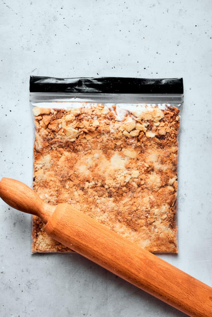 A wooden rolling pin crushes a Ziploc bag of pastry.