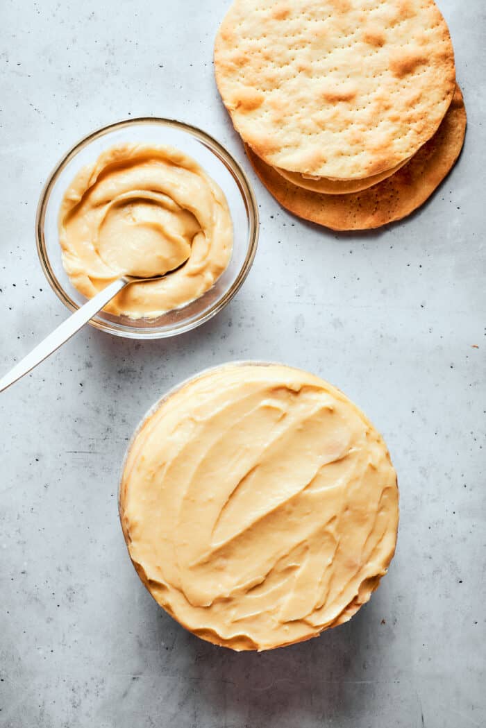 A bowl of pastry cream next to a Napoleon cake and a stack of pastry rounds.