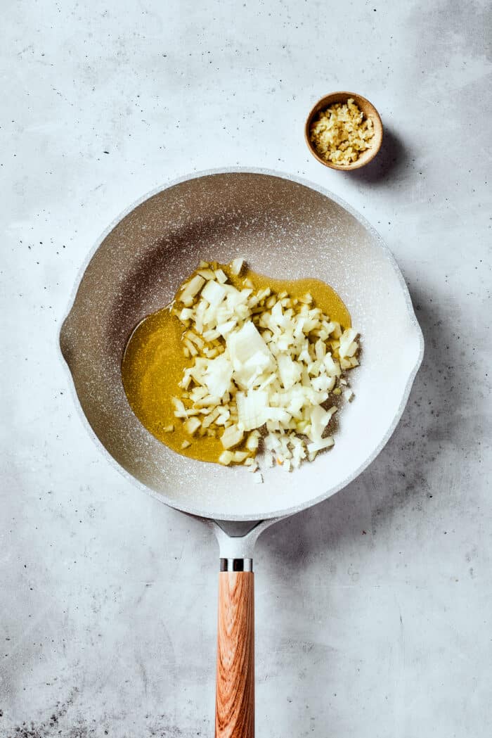 Onions and olive oil are shown in a white skillet.