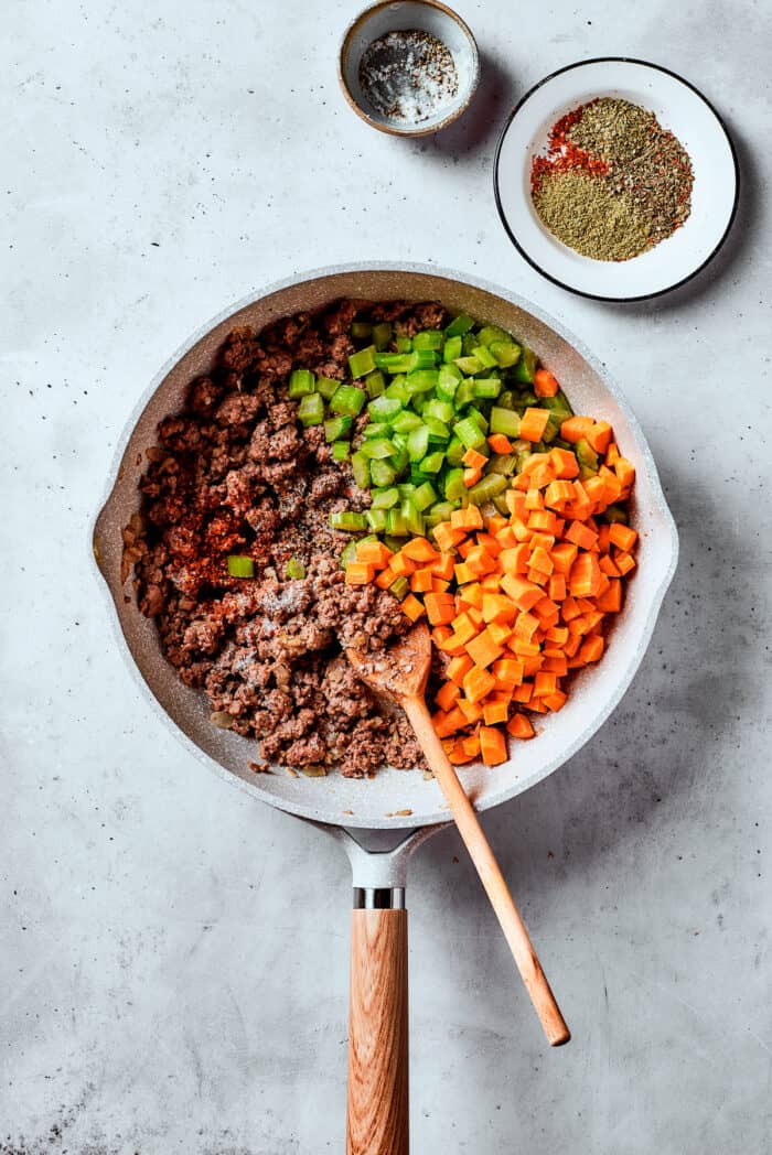 Carrots and celery are added to meat in a skillet.