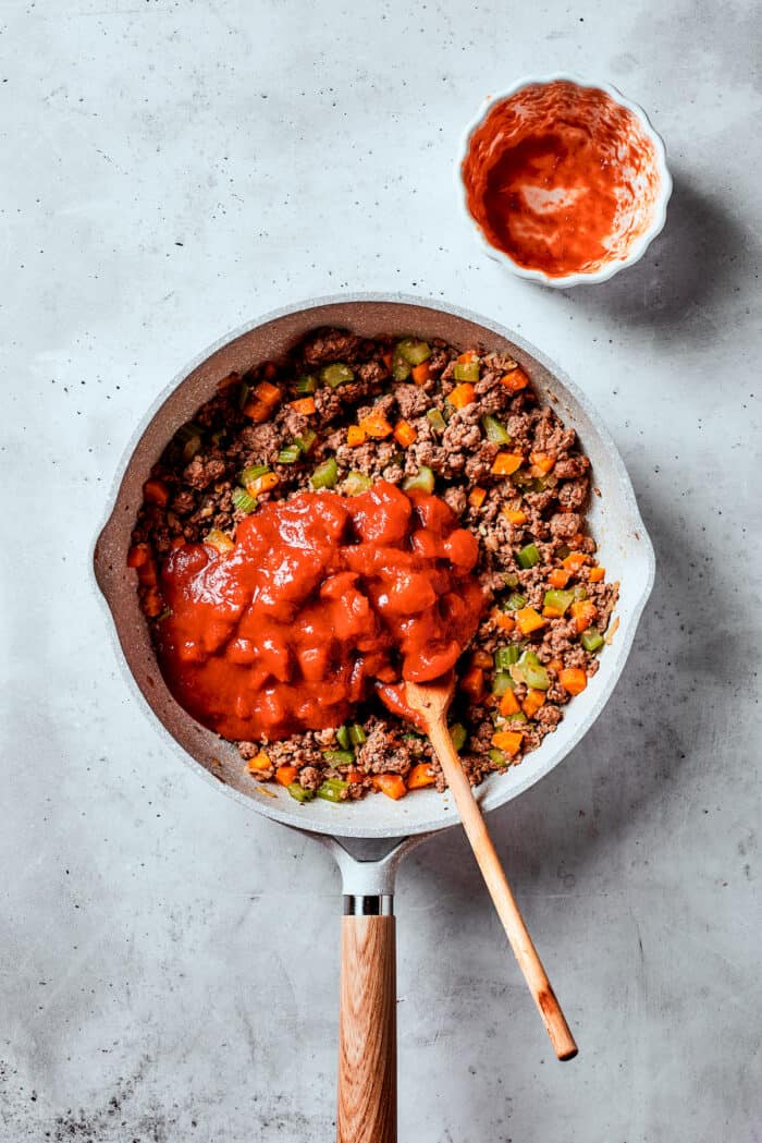 Diced tomatoes are added to a skillet f meat and vegetables.