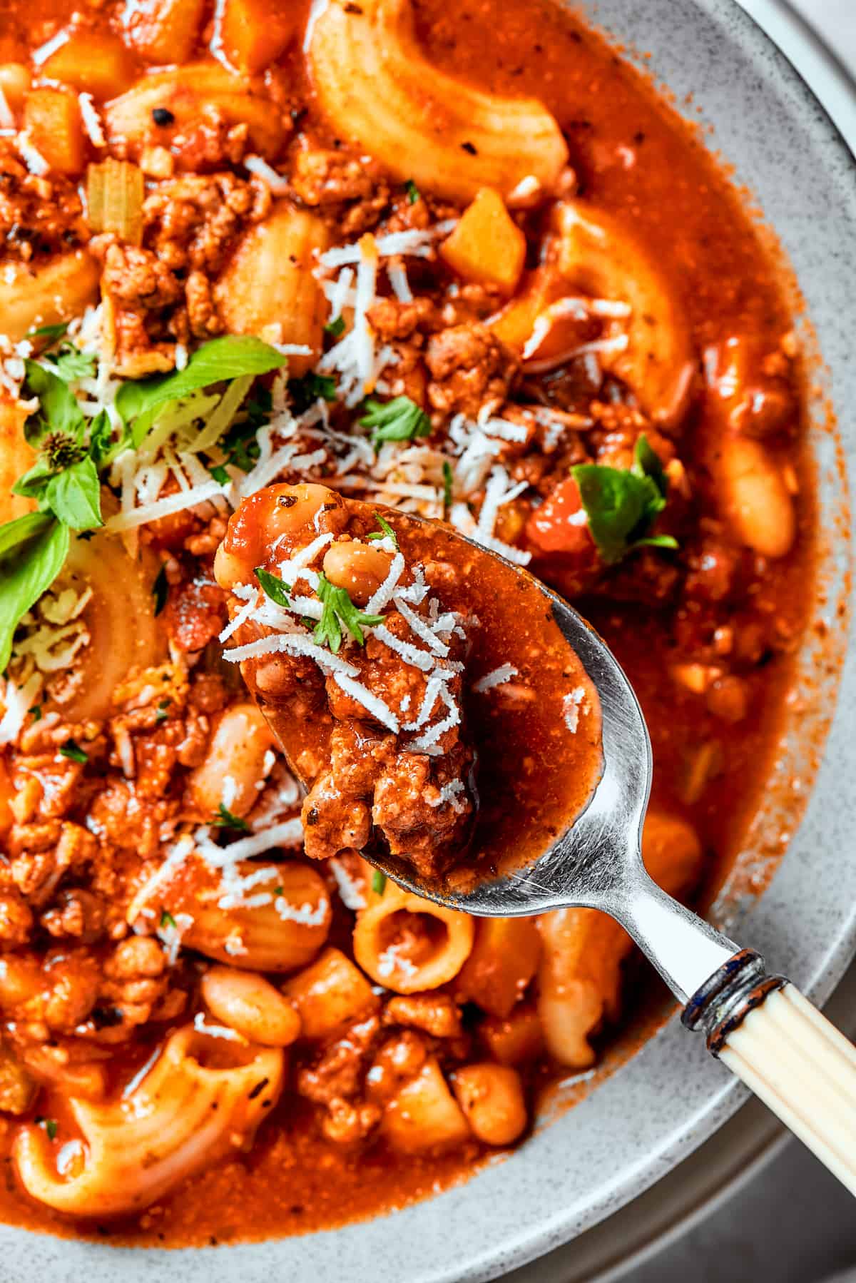 A spoon holds pasta fazool over a bowl.