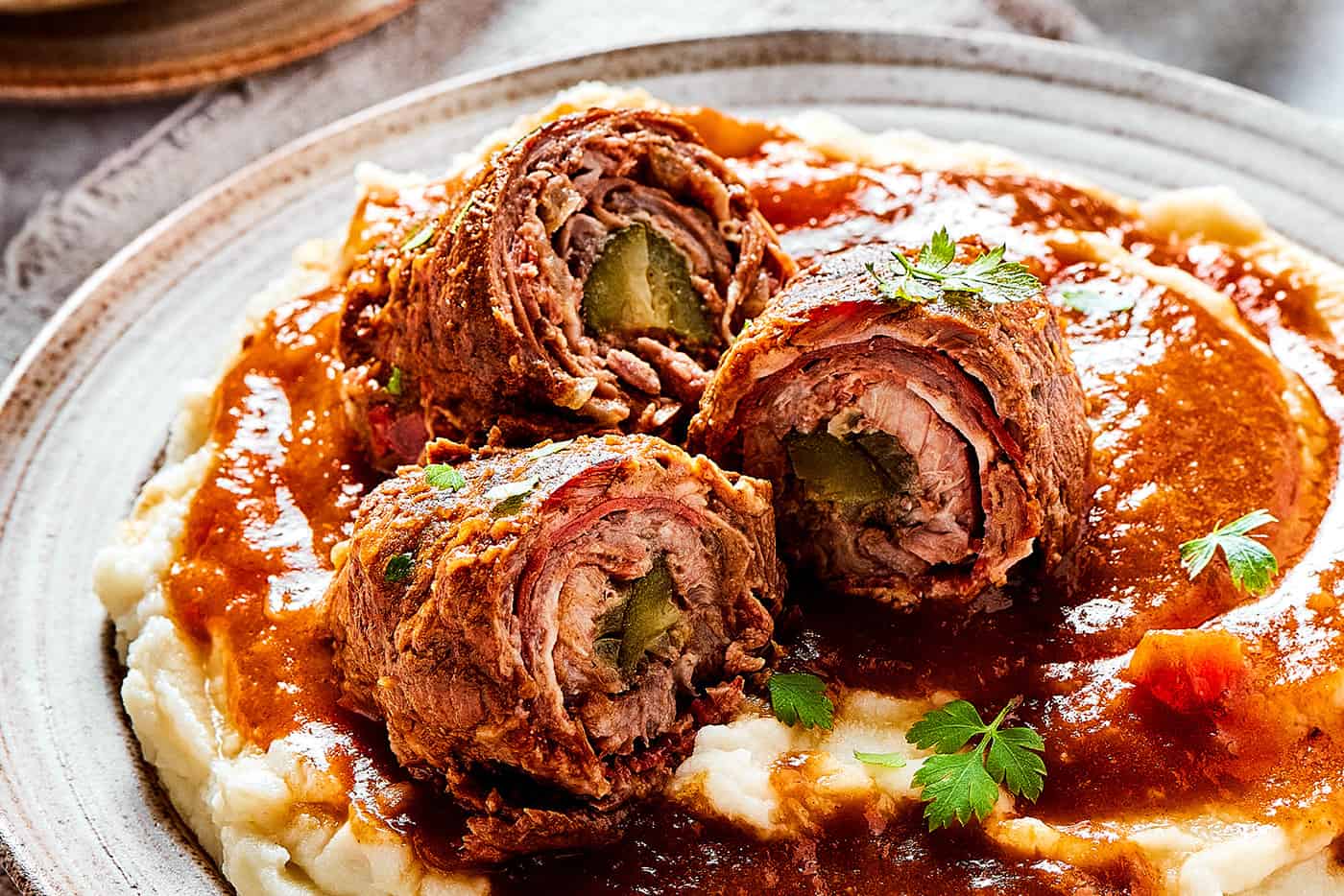 mashed potatoes, gravy, and pieces of rouladen sliced open to reveal the rolled-up interiors