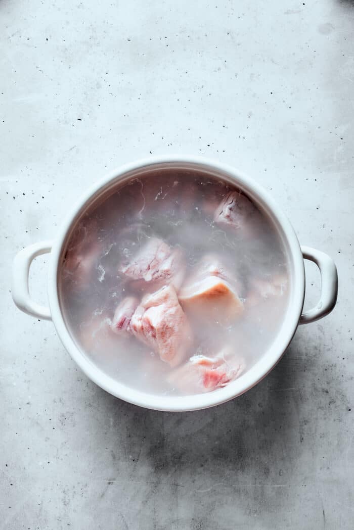 A top down shot of pork cooking in a white pot.