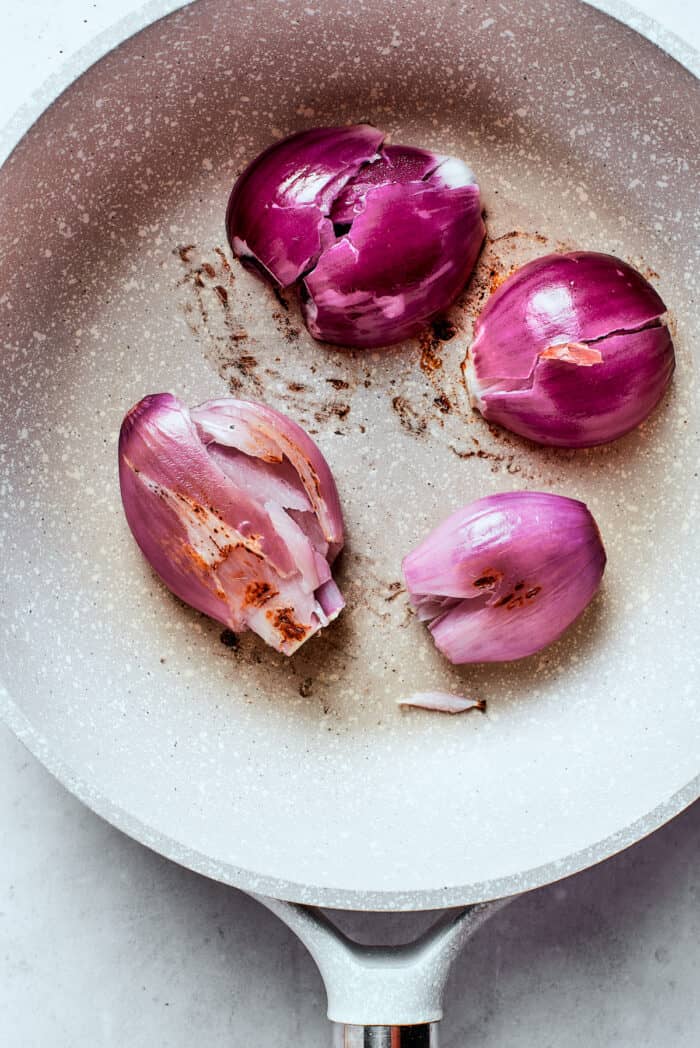 Shallots cook in a white skillet.