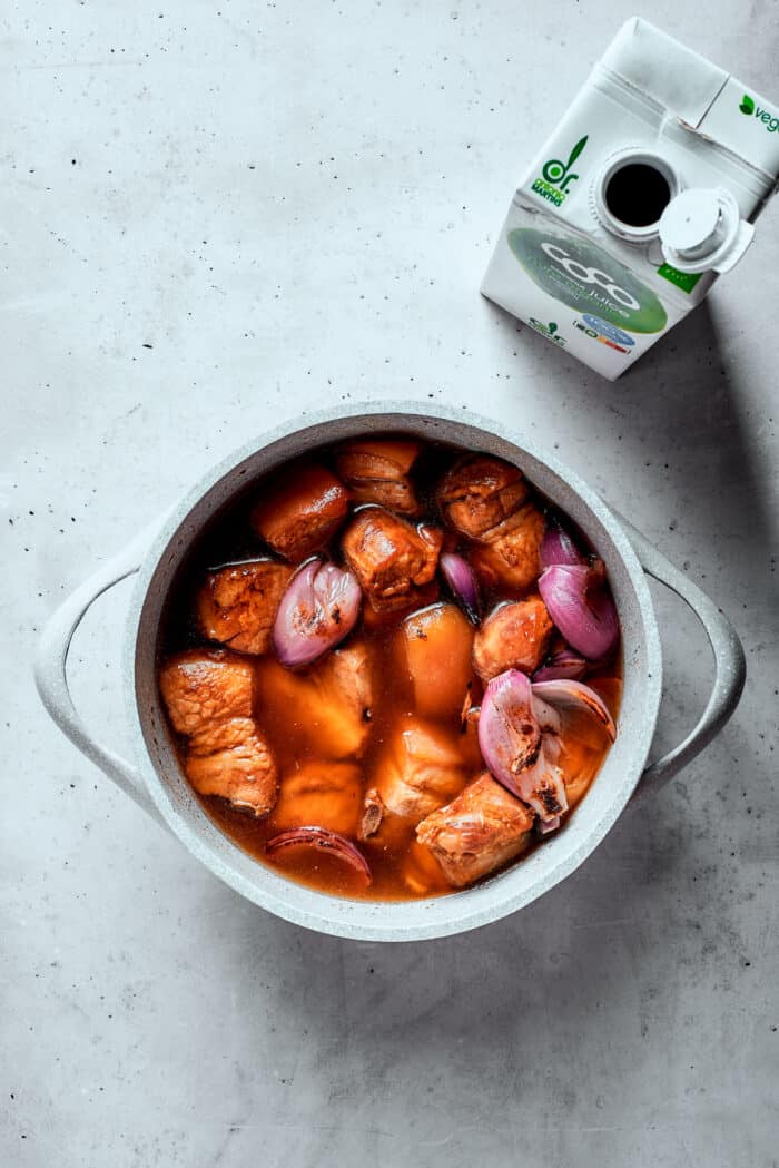 A pot of braised pork with a carton of coconut water next to it.