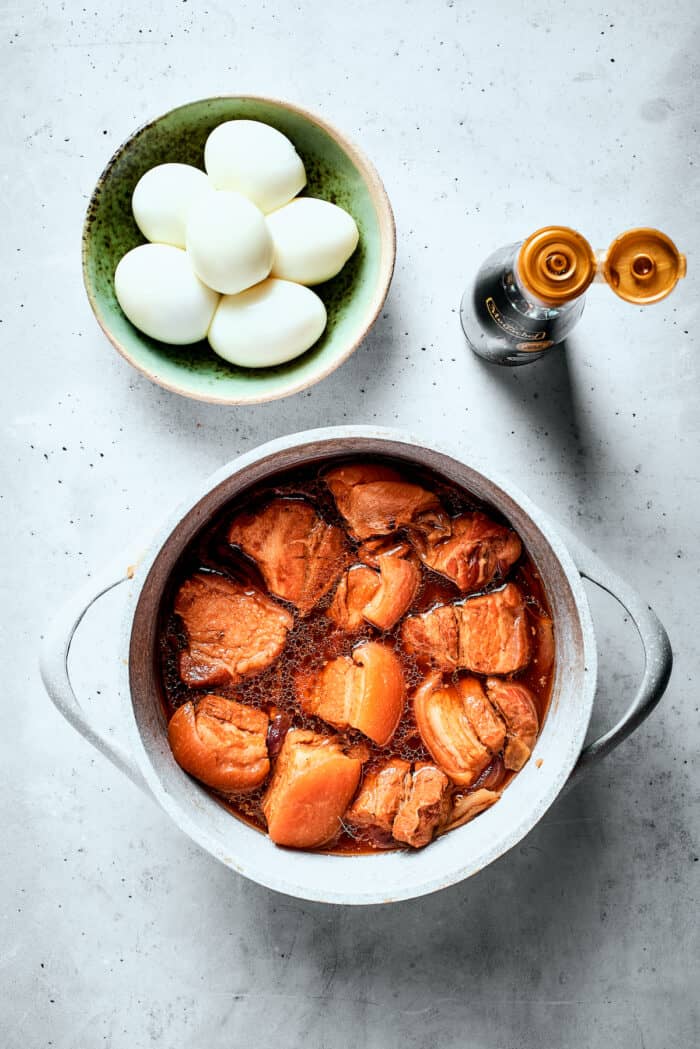 Braised pork in a pot is shown next to a bowl of hard boiled eggs.