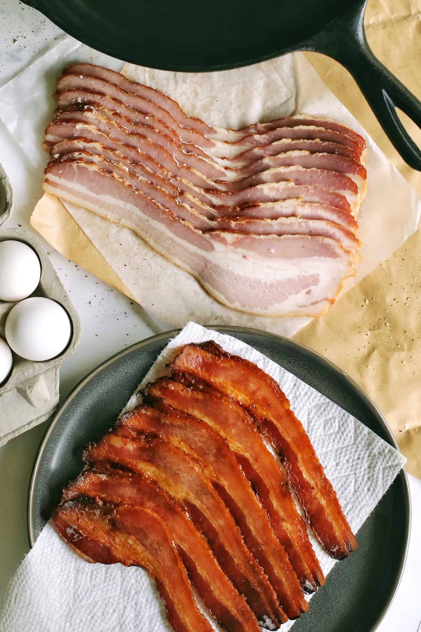 a cast iron skillet, cooked bacon, uncooked bacon, and a carton of eggs