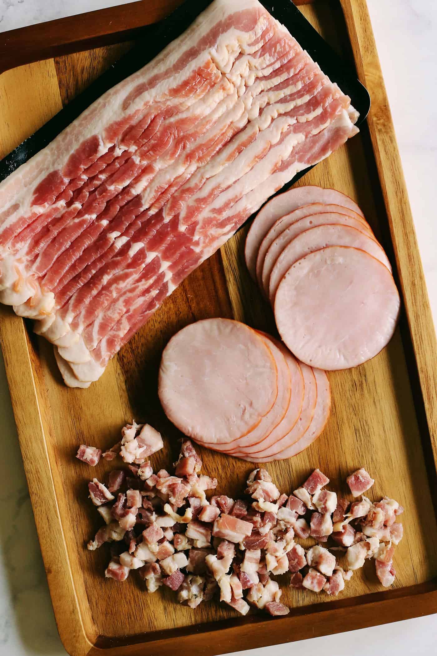 a wooden tray with Canadian bacon, bacon, and diced pancetta