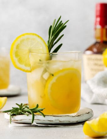 A glass of bourbon limoncello cocktail garnished with a lemon wheel and a sprig of fresh rosemary.