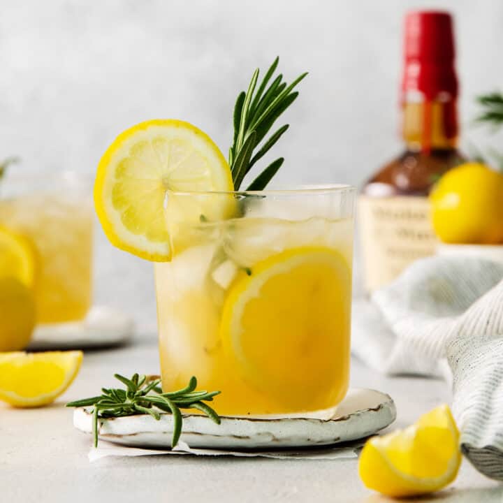 A glass of bourbon limoncello cocktail garnished with a lemon wheel and a sprig of fresh rosemary.