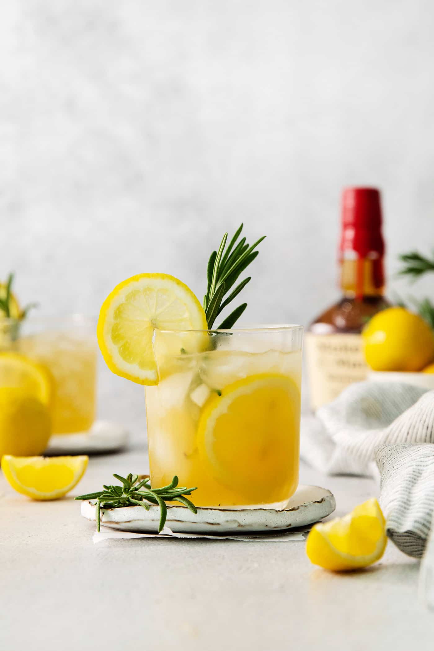 A glass of bourbon limoncello cocktail garnished with a lemon wheel and a sprig of fresh rosemary.