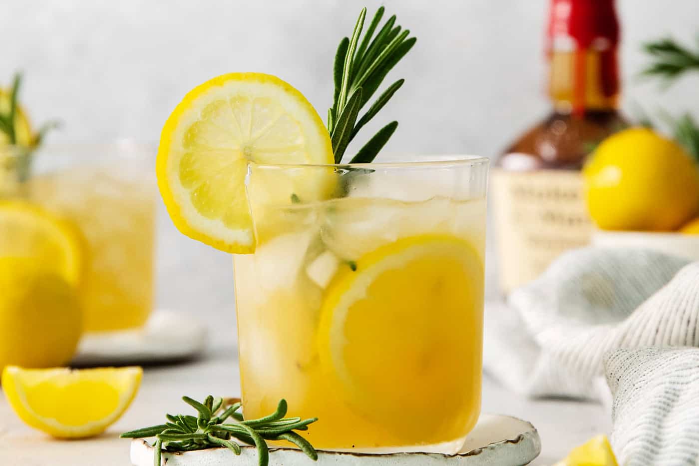 A glass of bourbon limoncello cocktail garnished with a lemon wheel and a sprig of fresh rosemary.