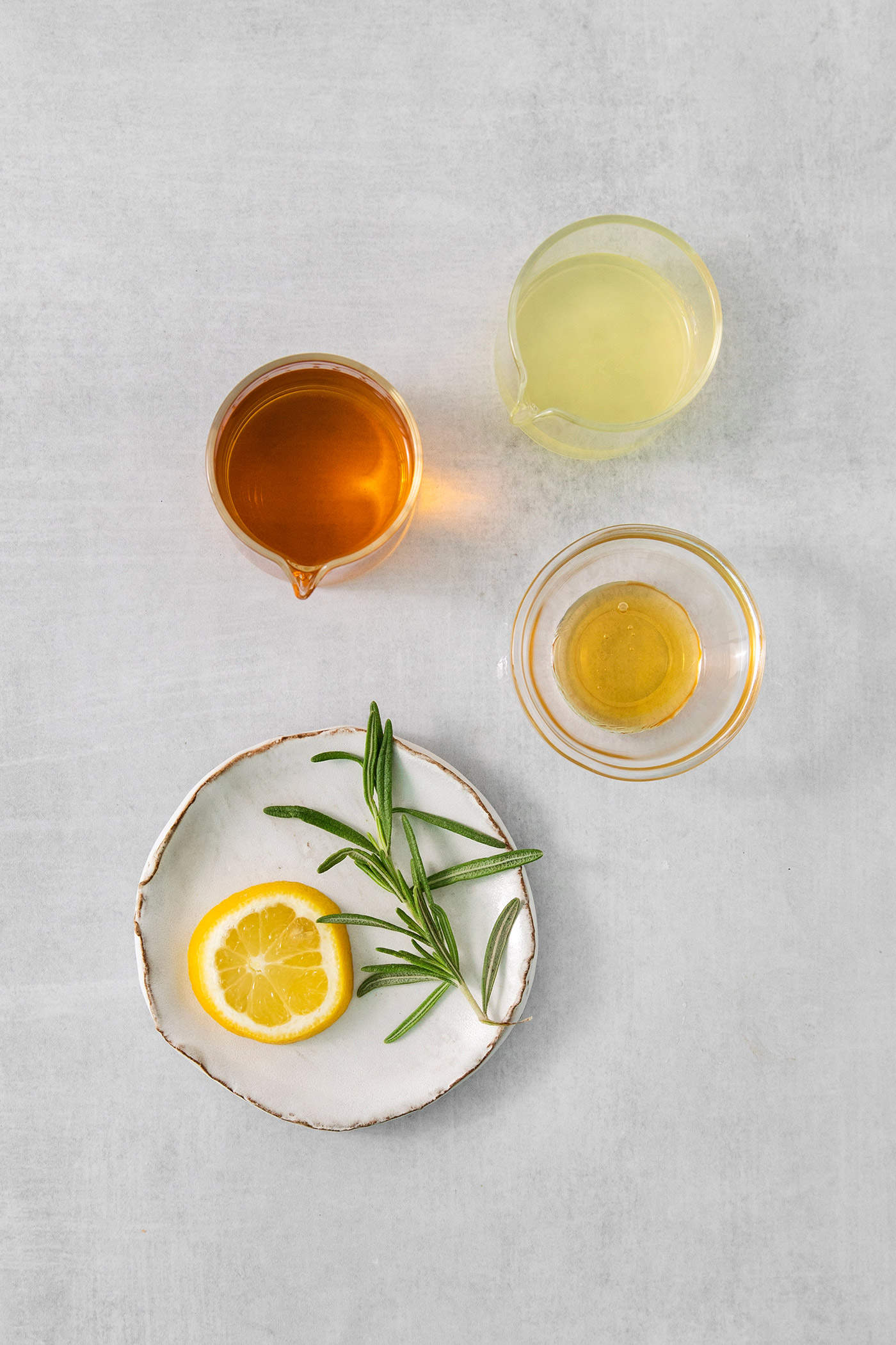 The ingredients needed to make bourbon limoncello cocktail are shown on a white background: limoncello, bourbon, honey, rosemary, and lemon.