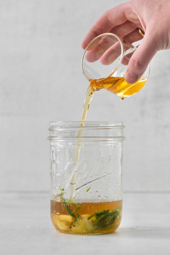 A hand pours bourbon into a glass jar for bourbon limoncello cocktail.