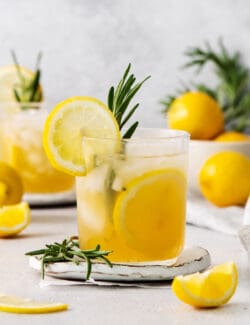 A glass of bourbon limoncello cocktail garnished with a lemon wheel and a sprig of fresh rosemary.