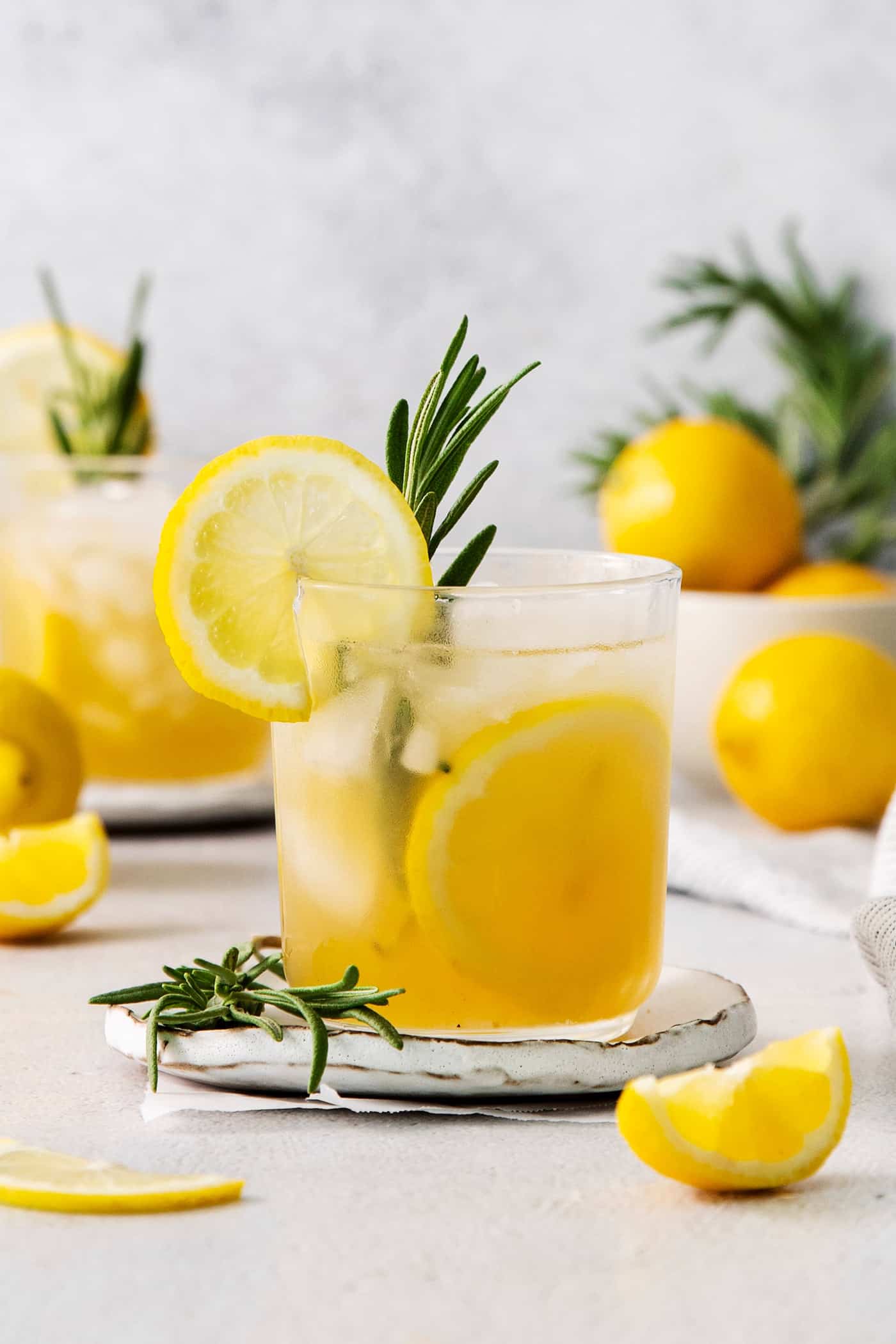 A glass of bourbon limoncello cocktail garnished with a lemon wheel and a sprig of fresh rosemary.