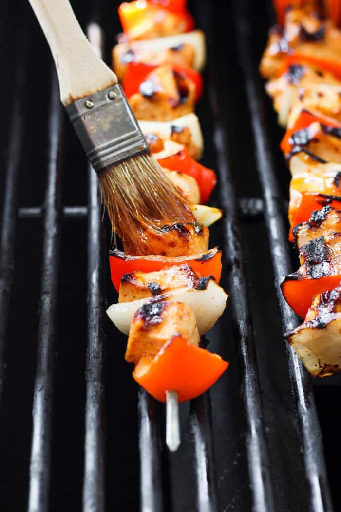 A marinade is brushed on chipotle honey chicken skewers as they cook on the grill.