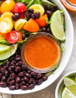 a jar of chipotle honey salad dressing inside a bowl of fresh salad with black beans