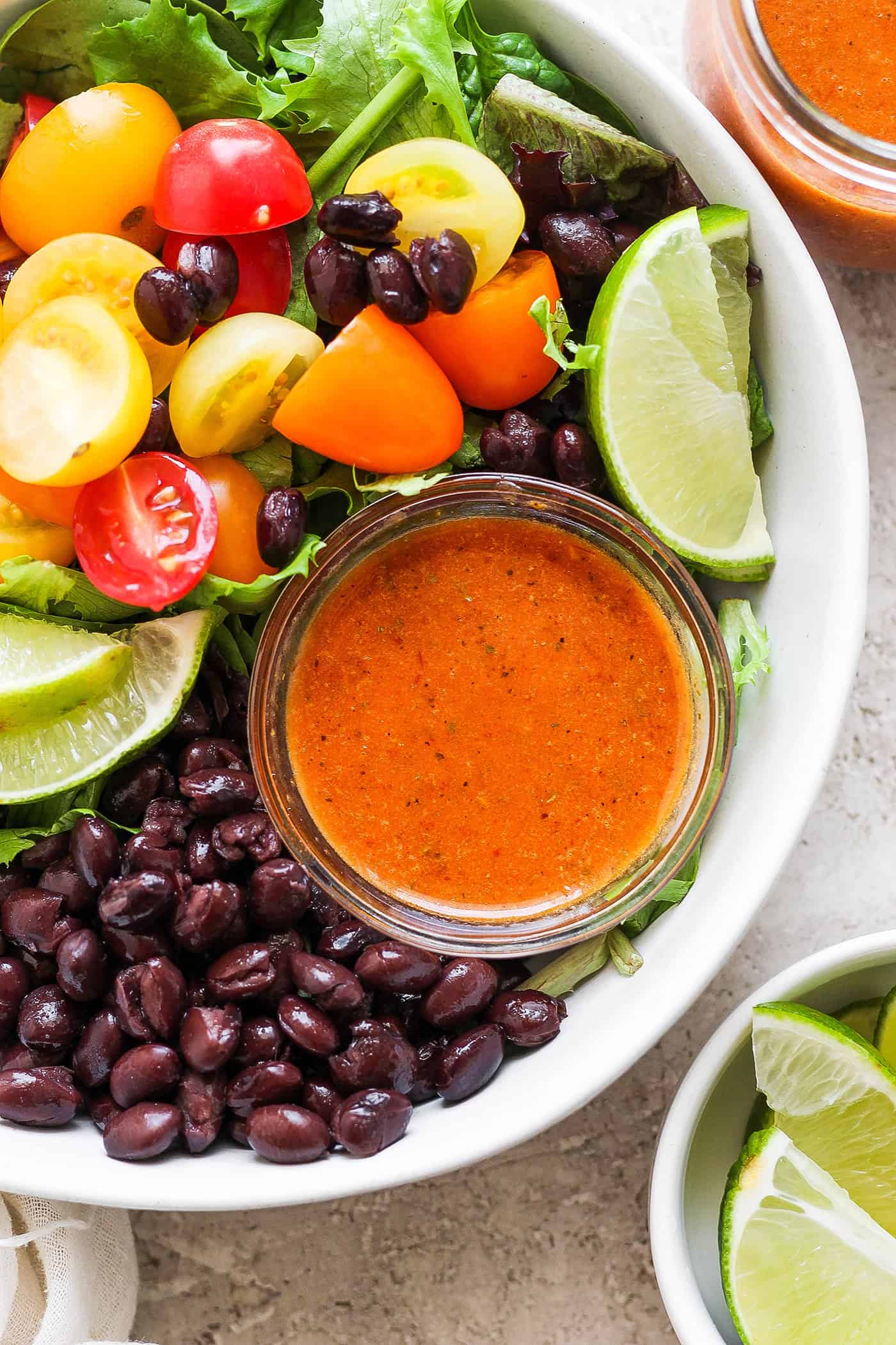 a jar of chipotle honey salad dressing inside a bowl of fresh salad with black beans