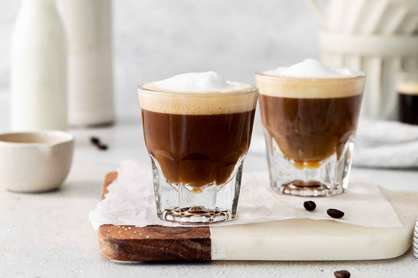 Two cortaditos are shown on a board with milk in the background.