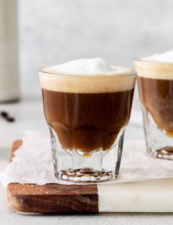 Two cortaditos are shown on a board with milk in the background.