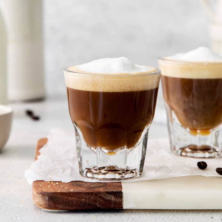 Two cortaditos are shown on a board with milk in the background.