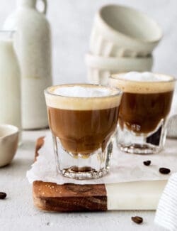 Two cortaditos are shown on a board with milk in the background.