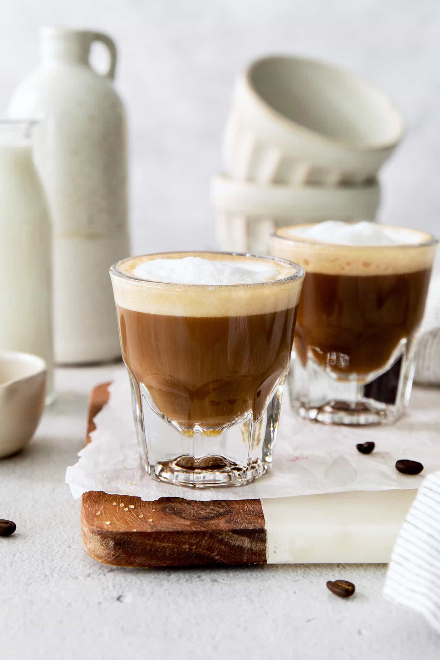 Two cortaditos are shown on a board with milk in the background.