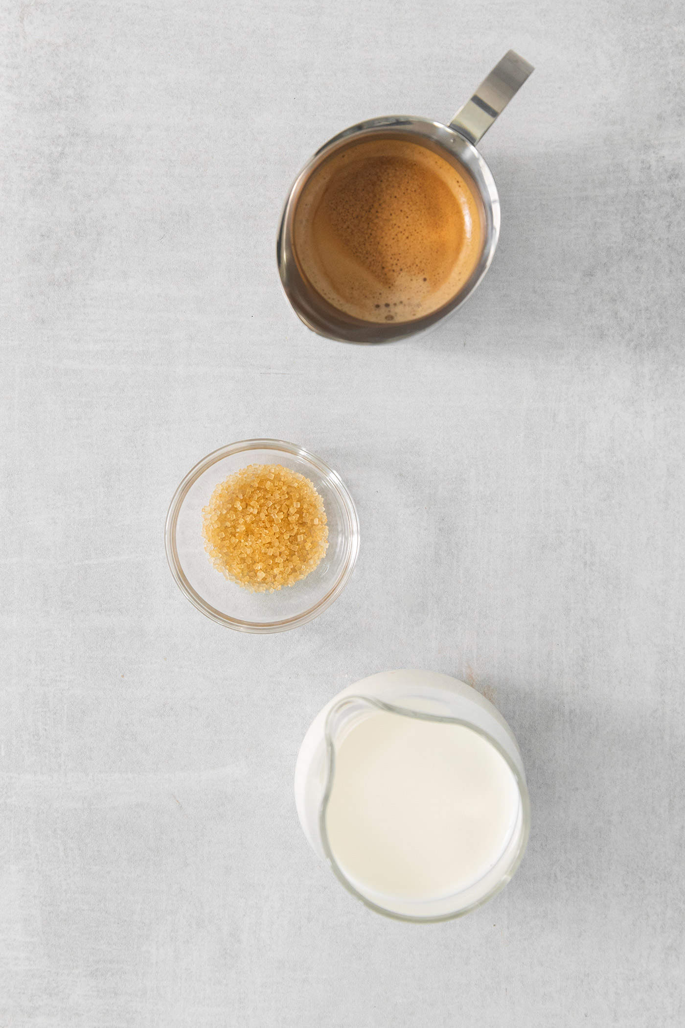 The ingredients for cortadito are shown on a white background: milk, sugar, and espresso.