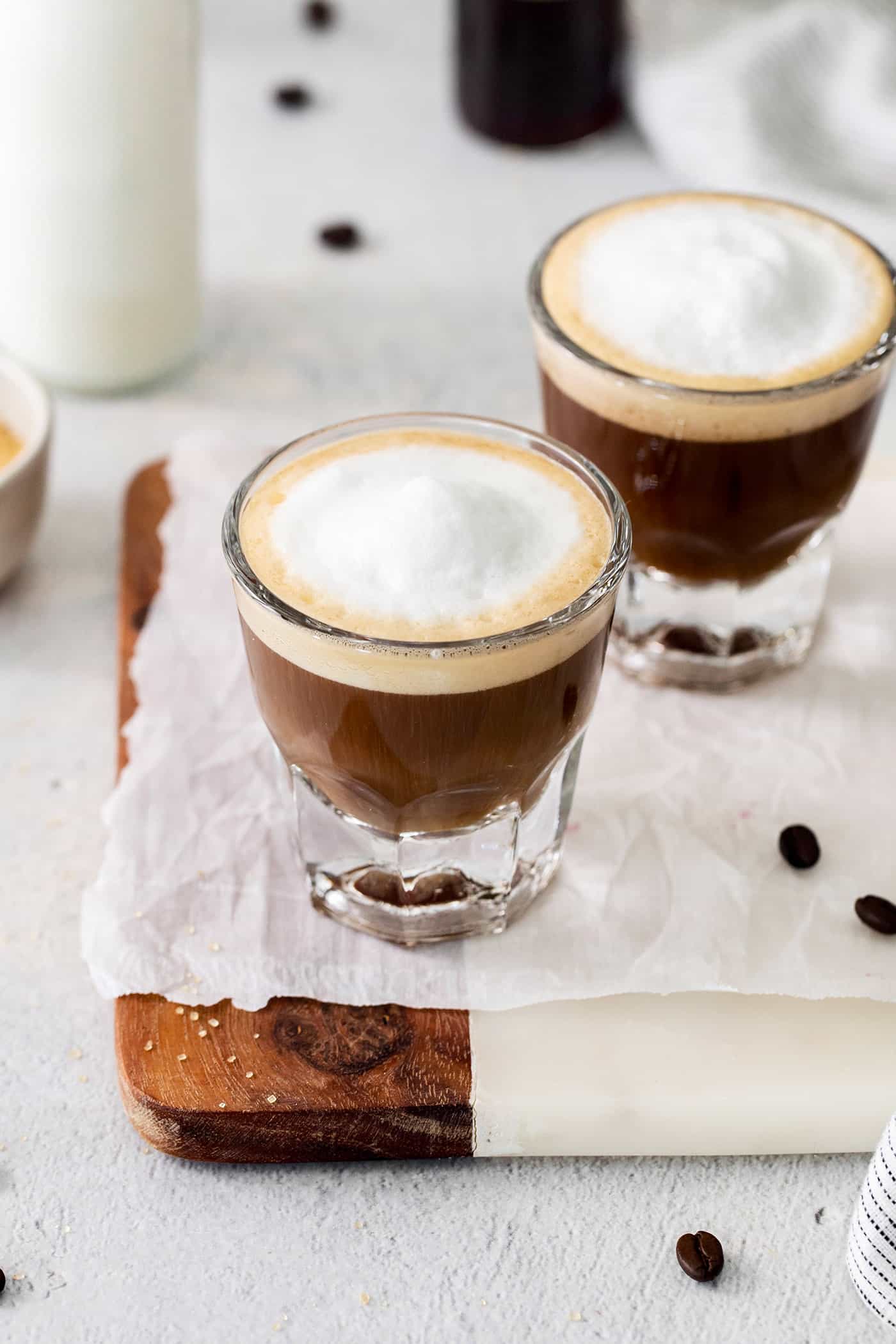 Two cortaditos are shown on a board with milk in the background.