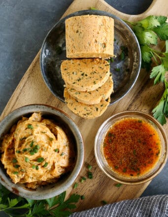 Cowboy butter on a wood board, shown 3 different ways: in a bowl, formed into a log, and melted