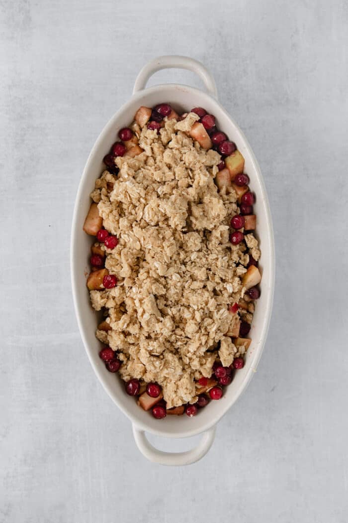 A white oval baking dish holds a baked cranberry apple crisp.