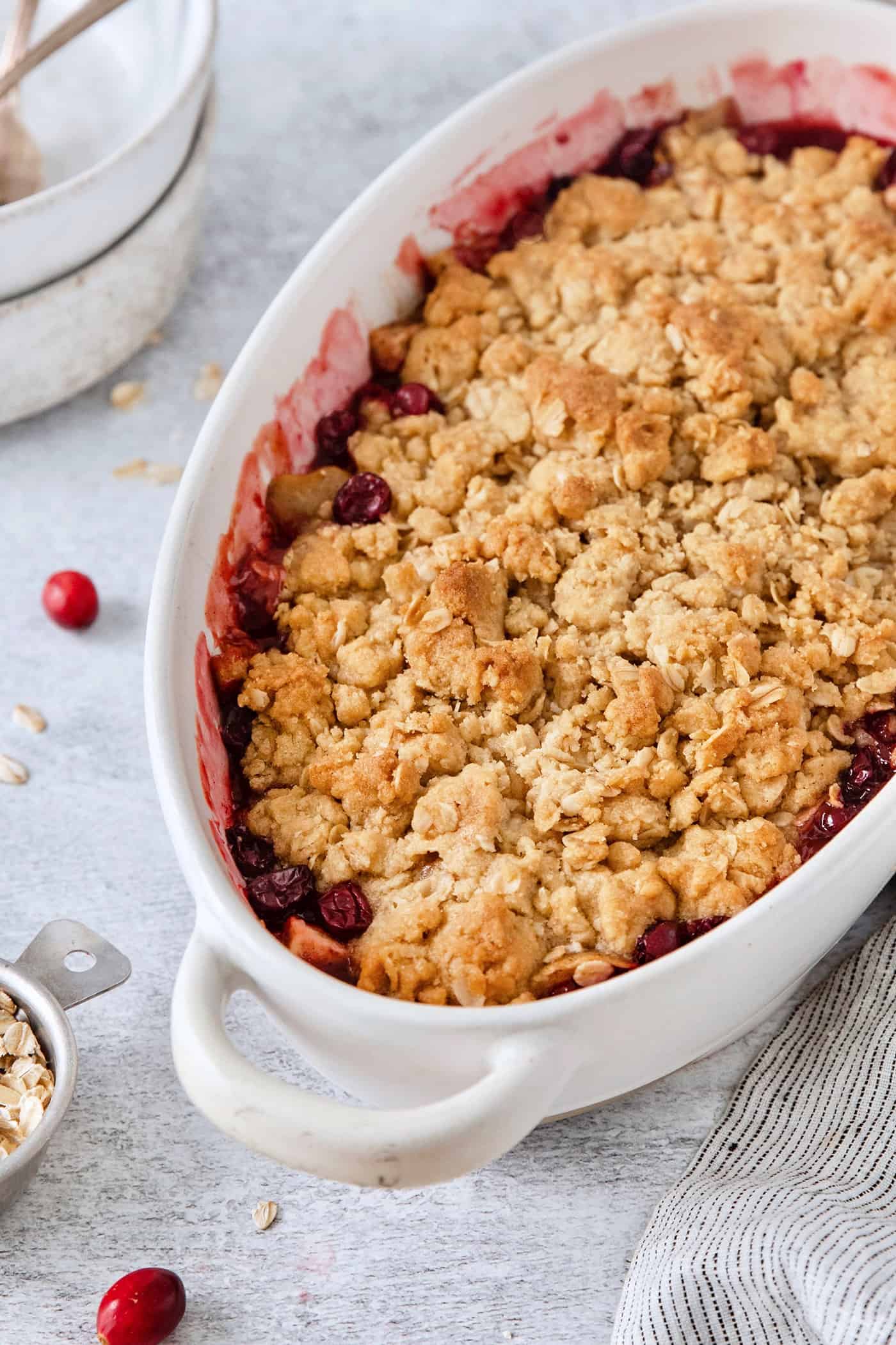 A white oval baking dish holds a baked cranberry apple crisp.