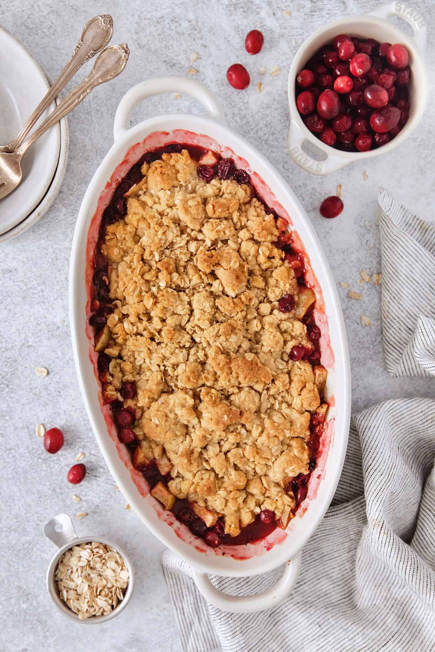 A white oval baking dish holds a baked cranberry apple crisp.