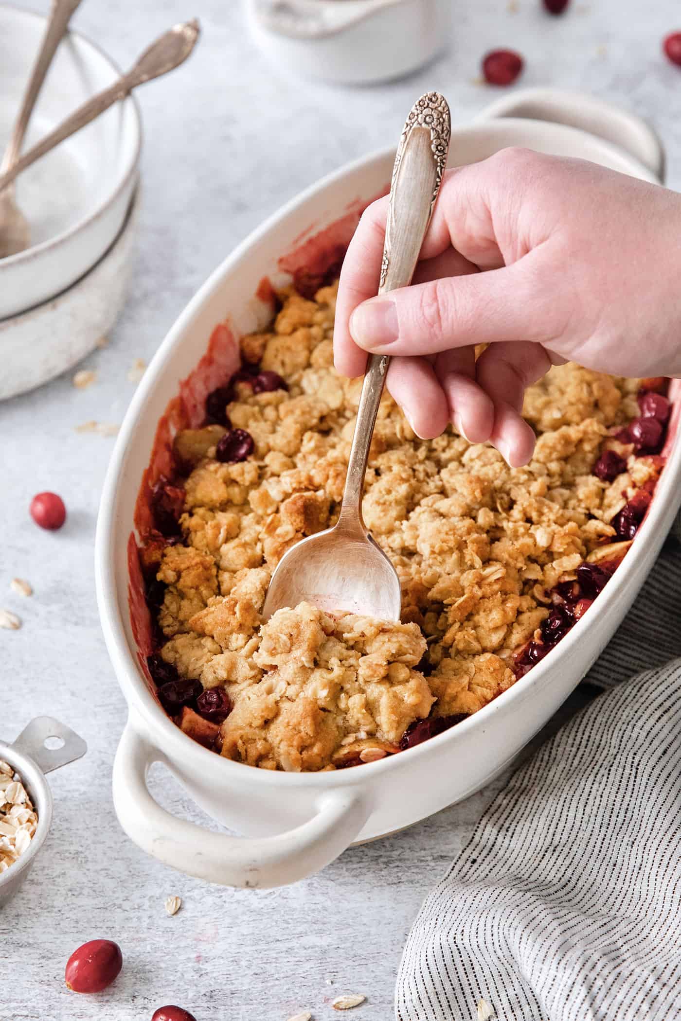 A hand holding a spoon cuts into a dish of cranberry apple crisp.