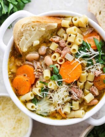 A bowl of Italian sausage soup with a slice of bread and cheese on the side.
