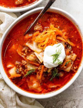 A bowl of unstuffed cabbage roll soup topped with carrot garnish and sour cream.