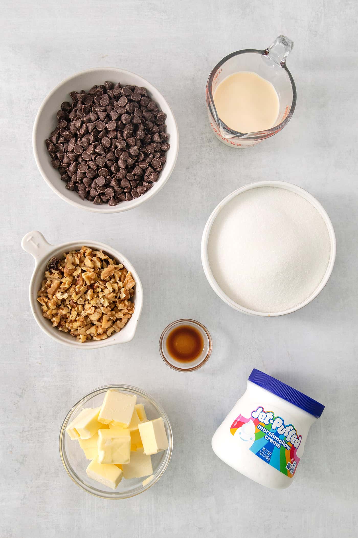 Ingredients needed for Fantasy Fudge are shown on a white background: chocolate chips, marshmallow creme, nuts, butter, sugar, and salt.