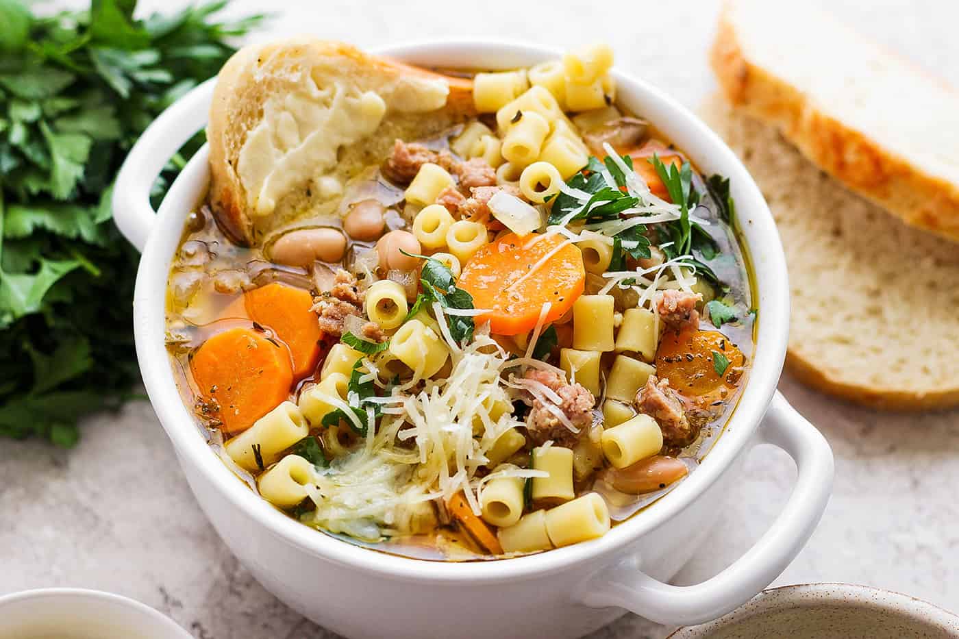 A bowl of Italian sausage soup with a slice of bread and cheese on the side.