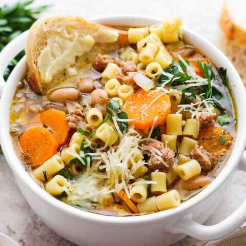 A bowl of Italian sausage soup with a slice of bread and cheese on the side.