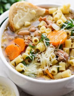 A bowl of Italian sausage soup with a slice of bread and cheese on the side.