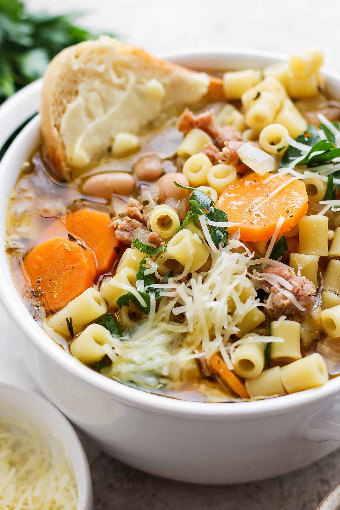 A bowl of Italian sausage soup with a slice of bread and cheese on the side.