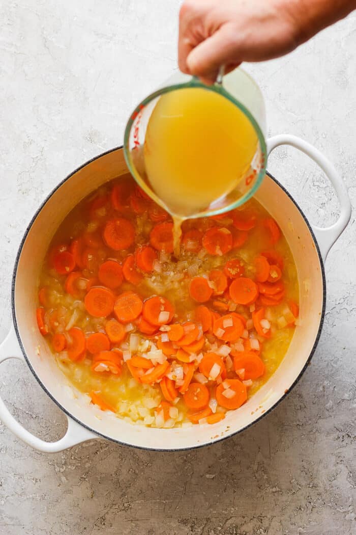 Broth is poured from a measuring cup into a pot with carrot coins.