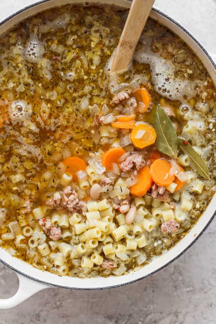 A close up shot shows a pot of Italian sausage soup with carrot coins and pasta.