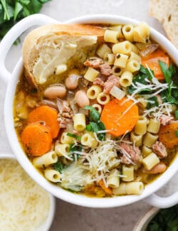 A bowl of Italian sausage soup with a slice of bread and cheese on the side.