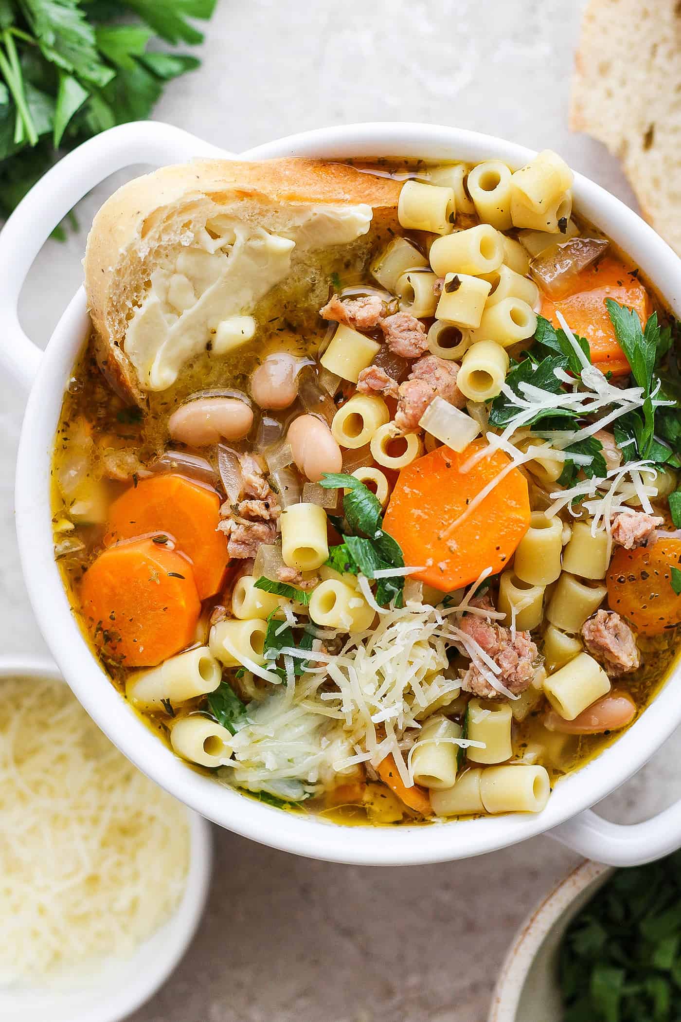 A bowl of Italian sausage soup with a slice of bread and cheese on the side.